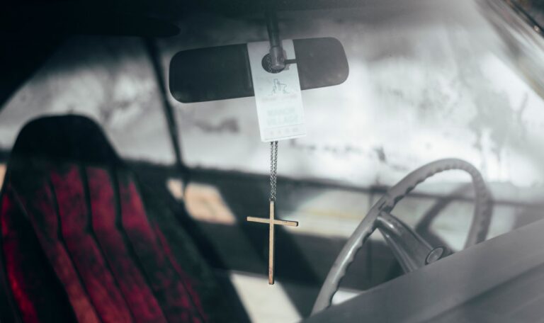 Cruz colgada del retrovisor de un coche, símbolo de protección para los conductores como San Cristóbal